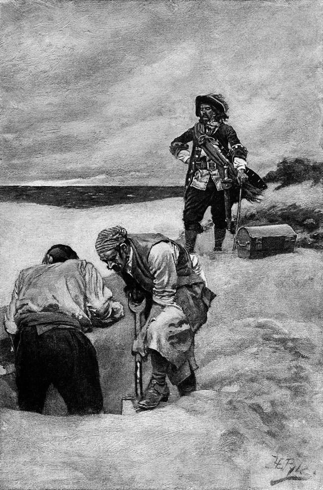 Black and white photograph of two men dressed as pirates digging a large hole on a sandy beach. Behind them another man dressed as a pirate, though better dressed with a captains hat stands with a sword and treasure chest next to him and watches.