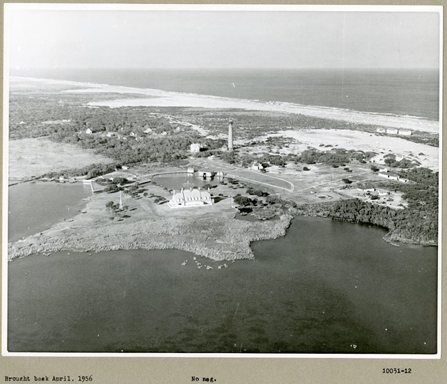 Black and white aerial of subdivision on the edge of the water with open space and many trees.