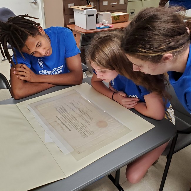 Three young teens in blue shirts examine paper