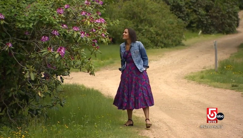 Woman walking on dirt path smelling a purple flower