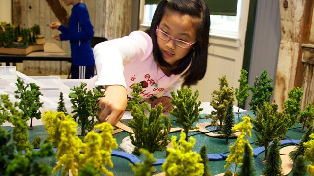 Young girl places miniature trees on model of park