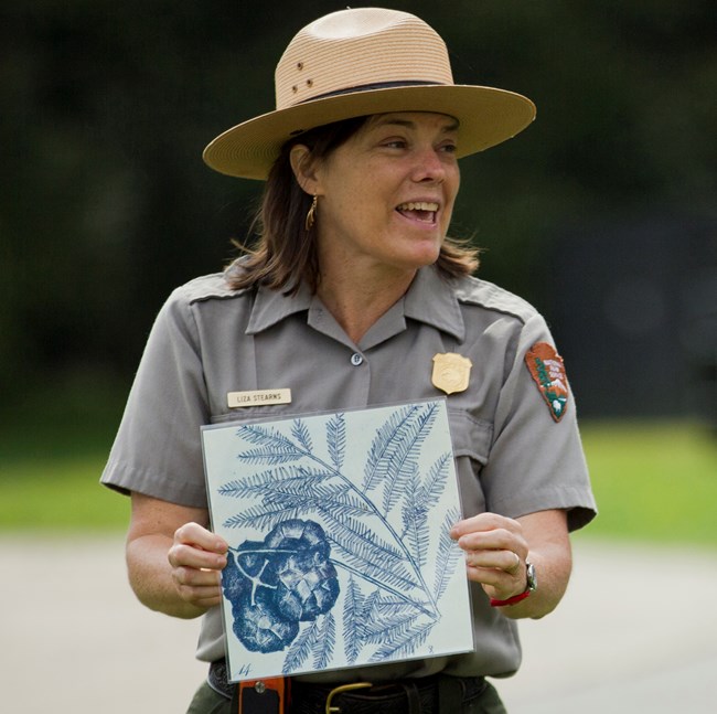 Park ranger in uniform with flat hat holds up image