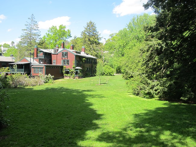 Large open lawn with house on far side and trees on edges.