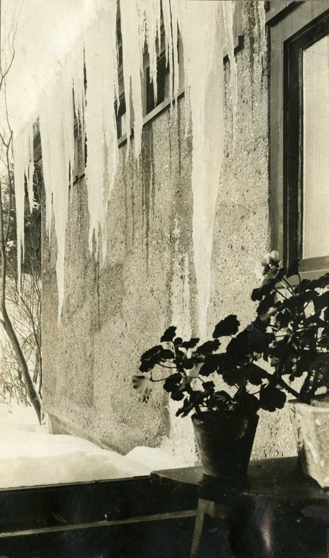 black and white view through window of large icicles coming off adjacent roof