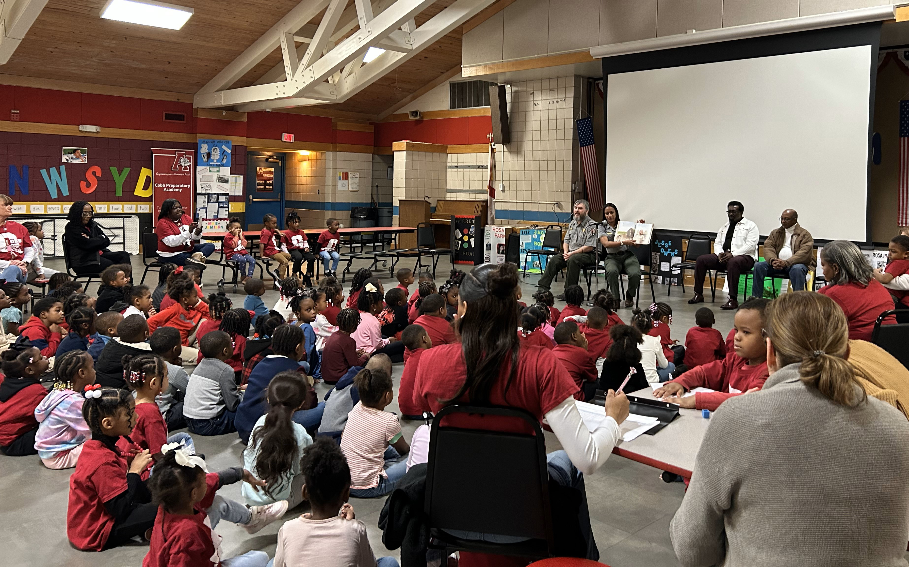 A group of students and teachers listen as rangers read a book