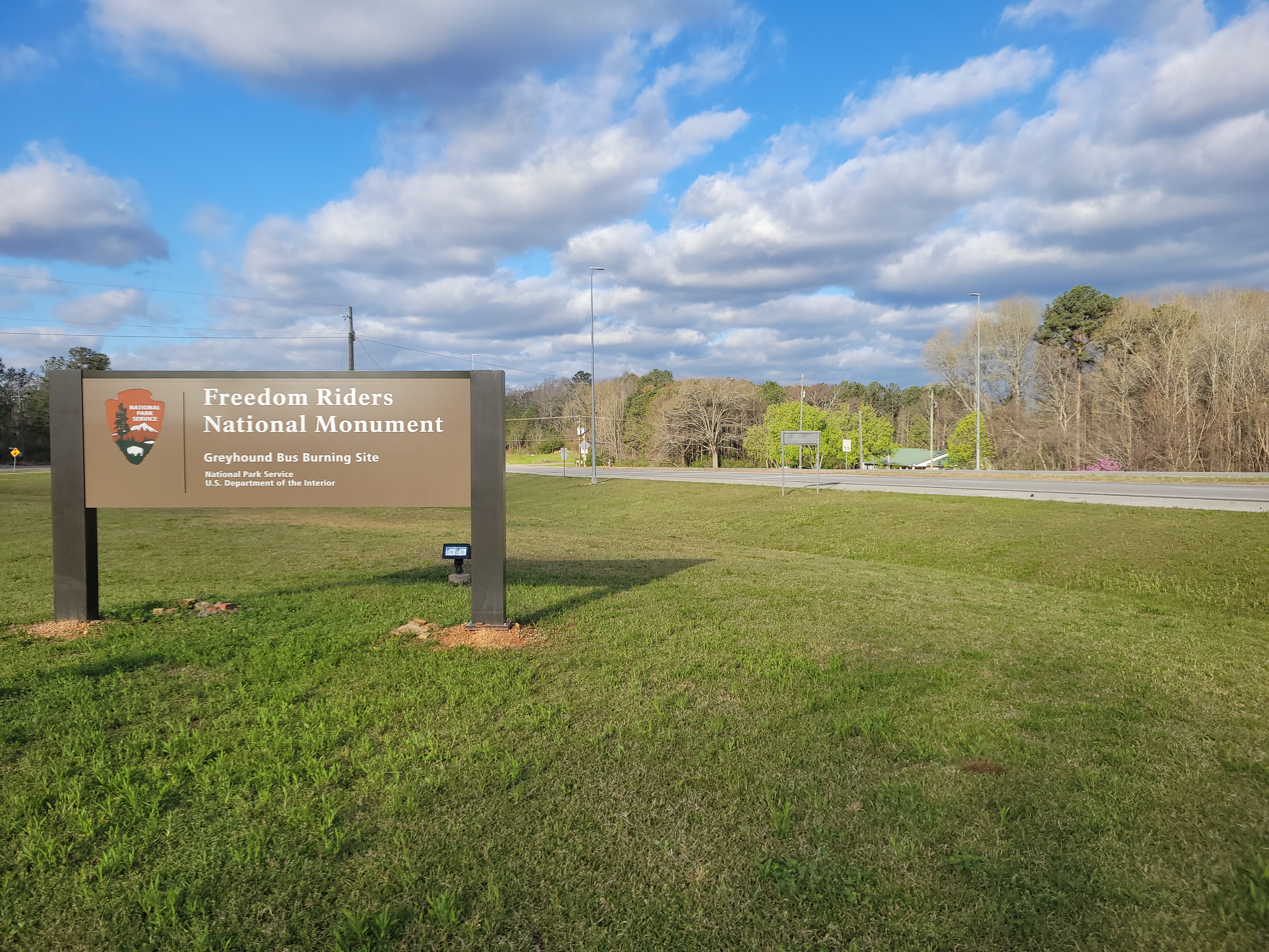 A sign saying Freedom Riders National Monument Greyhound Bus Burning Site is posted in a field along Highway 202 outside Anniston Alabama.