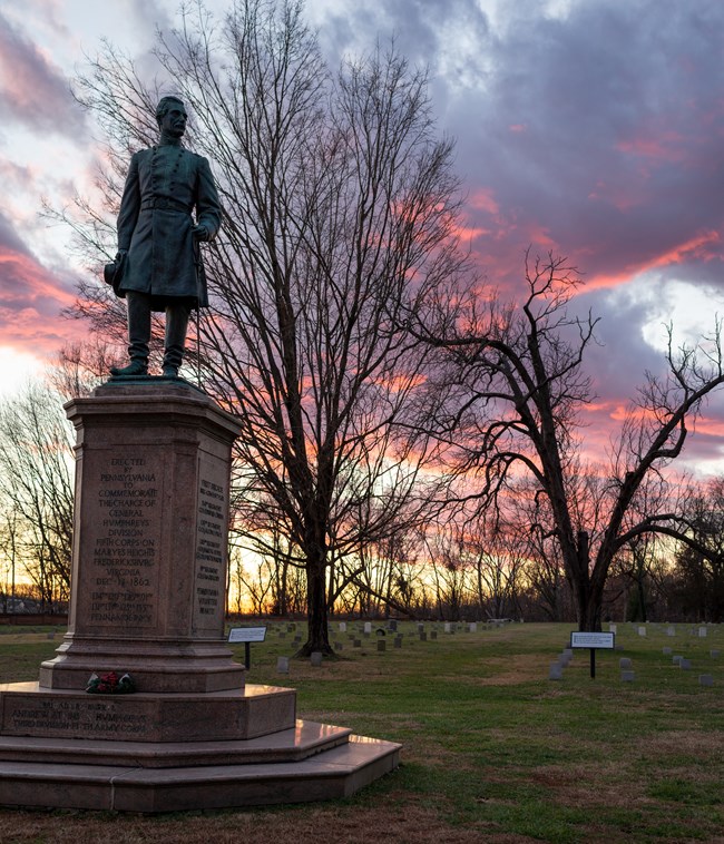 A statue of a Civil War general in stone in a cemetery at sunset.