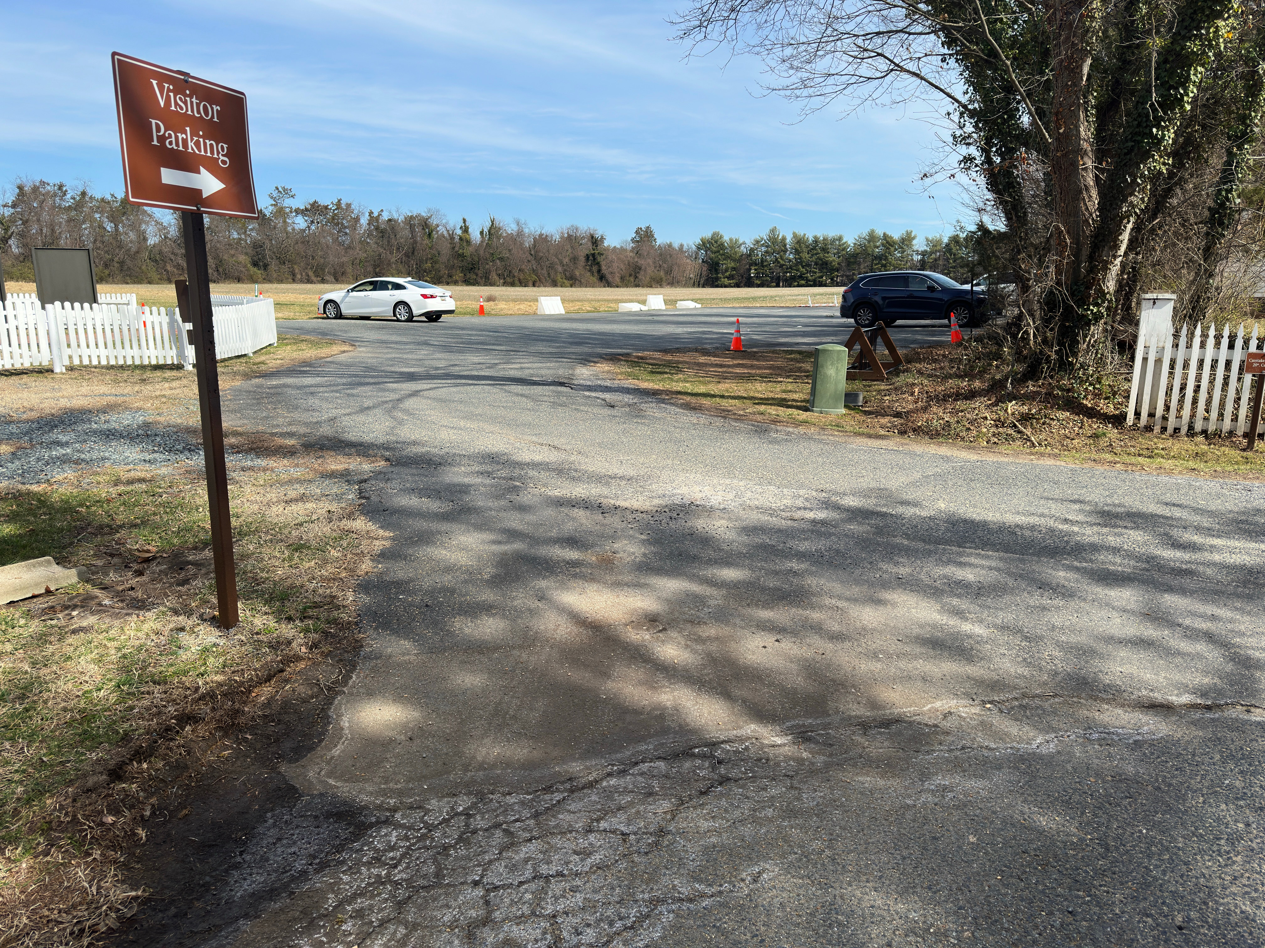 A visitor parking sign in front of a parking lot with cracks and potholes.