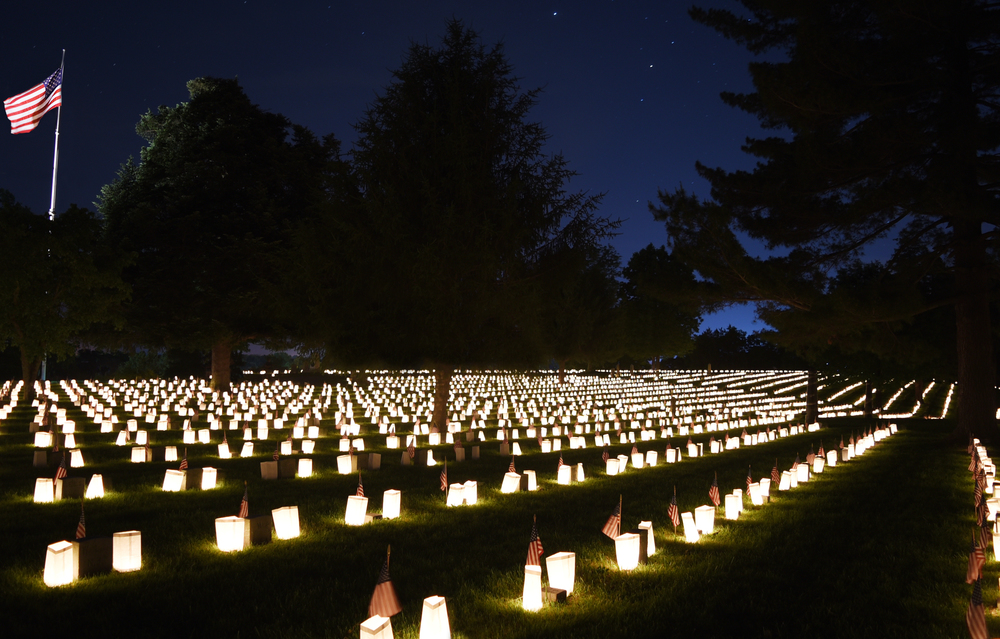 Photo taken of the Fredericksburg National Cemetery at night with small luminaries on each grave and the U.S. flag in the background