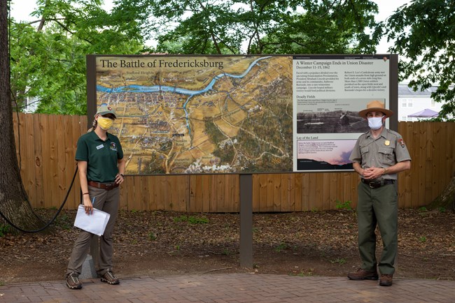 Two park employees in face coverings standing next to a large battle map.