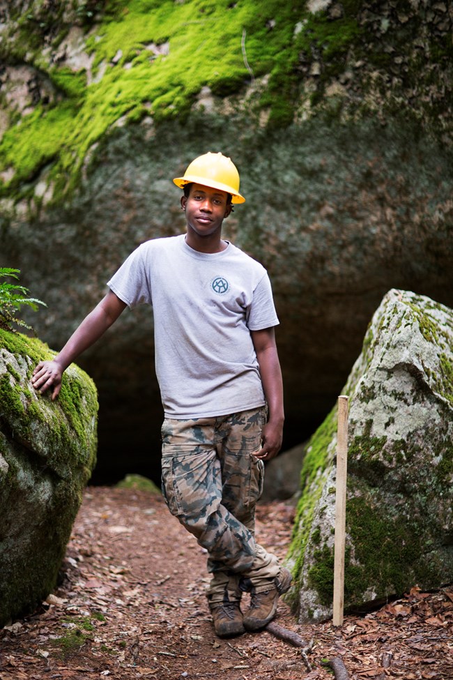 A man poses for a photo between two large boulders on a trail.