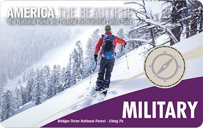 America The Beautiful Military Pass; A man in a red jacket, skiing along a snowy mountainside.
