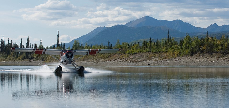 A floatplane lands on a lake in front of a distant mountain