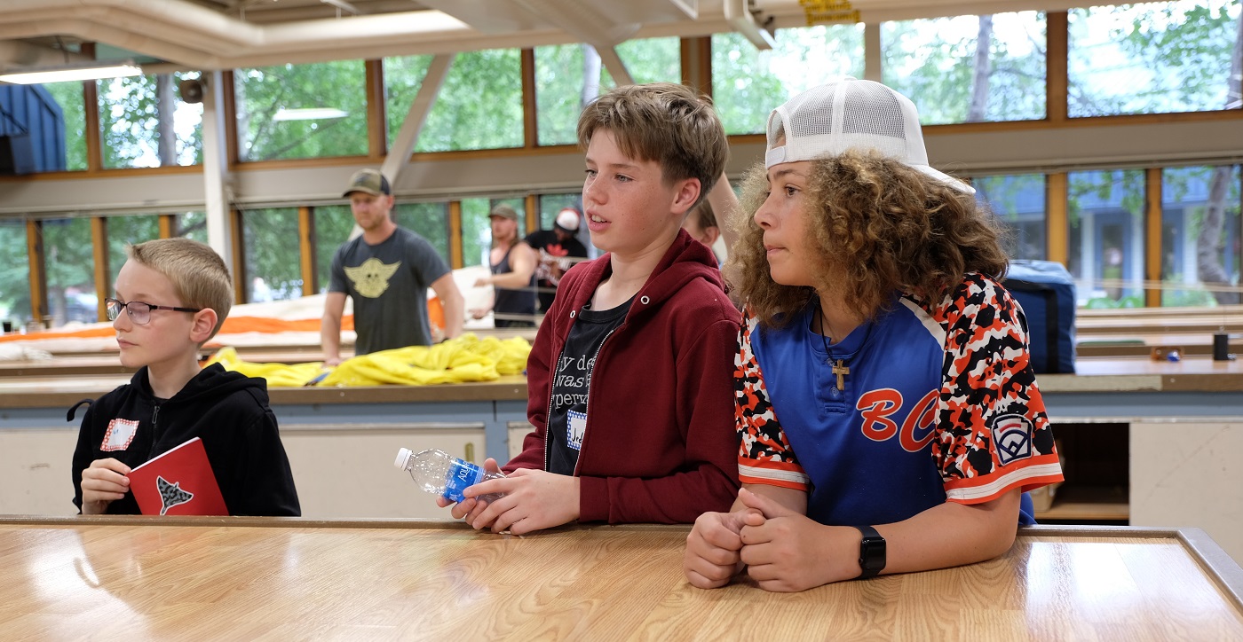 Three students stand at a work station.