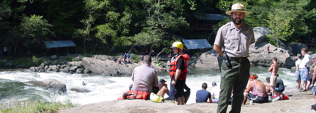 ranger standing by river with rafters