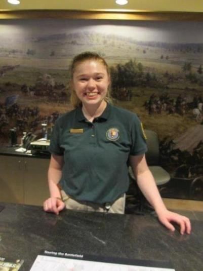 An intern smiles while providing information to visitors while working at the Park Visitor Center's Information Desk