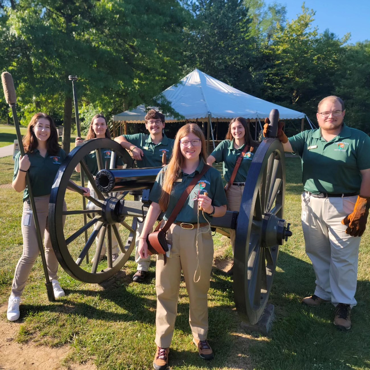 Interns wearing green shirts pose with artillery implements near a Civil War cannon