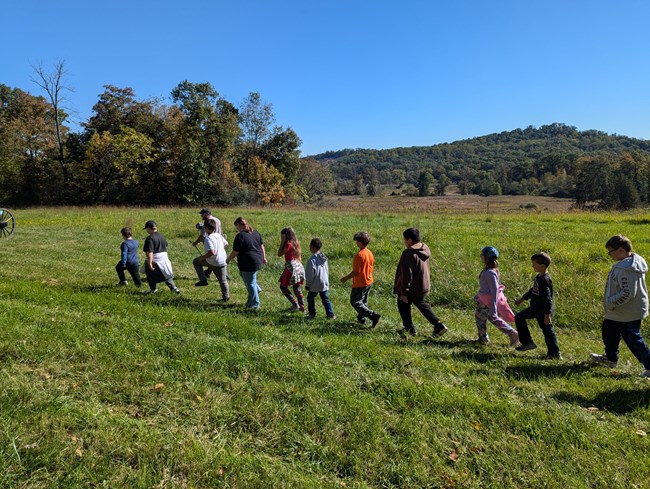 Children wlak in a line behind a ranger in a grassy field