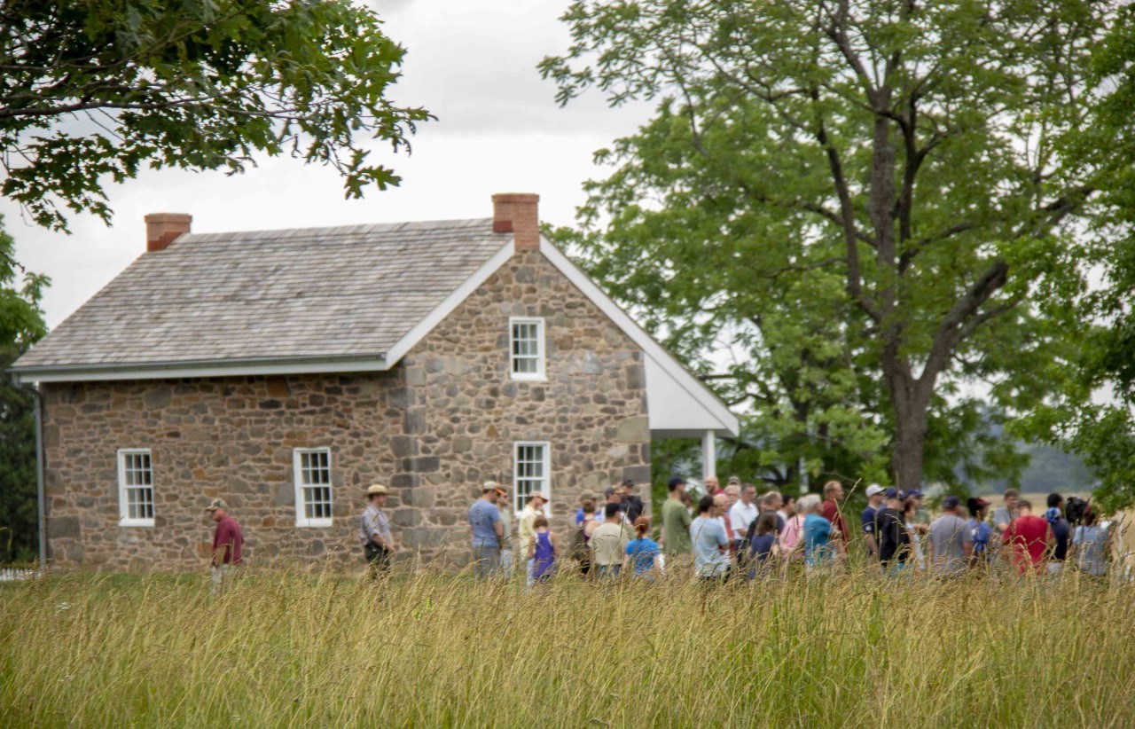 A group of visitors stand near the stone Warfield house on the Gettysburg Battlefield.