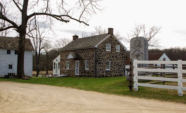 Photograph of the stone one-and-a-half story home of the Slyder Family with wooden farm outbuildings; a granite monument is in the foreground