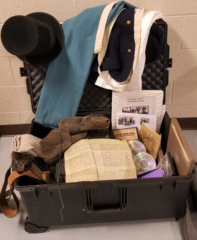 An opened Traveling Trunk reveals items a Civil War soldier would have worn and carried, along with a stovepipe hat and Civil War books.