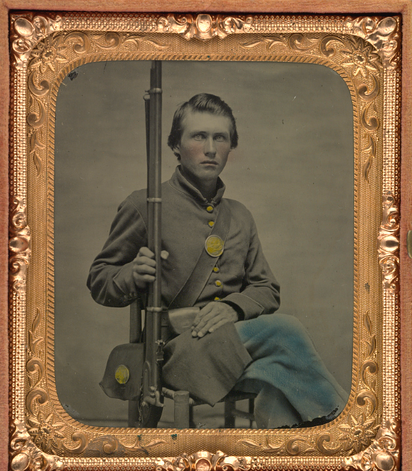 Photograph of a seated U.S. Civil War soldier holding a musket, looking directly at camera