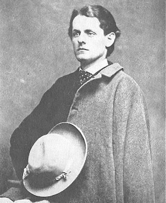 Black and white photograph of a man in a long coat holding a hat
