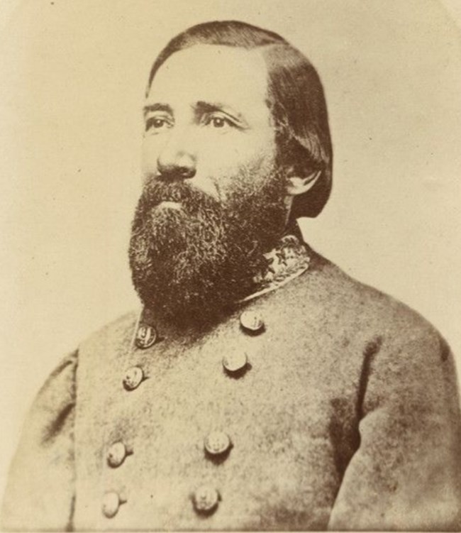 Black and white photograph of a bearded man with black hair wearing a gray military coat