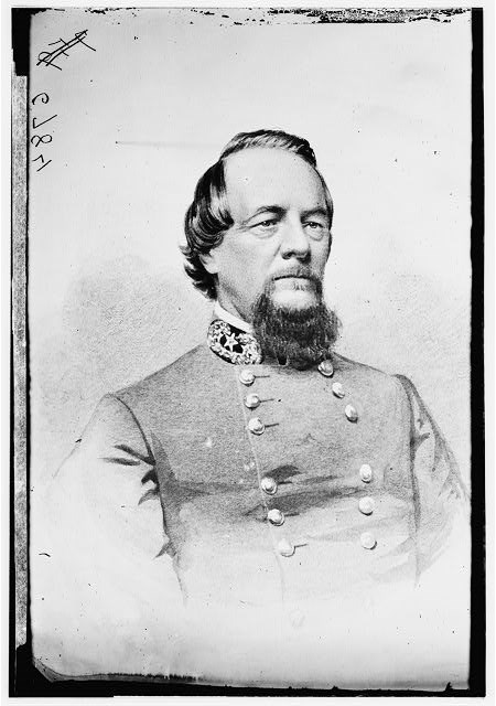 Black and white photograph of a man with dark hair and a beard in a gray military uniform