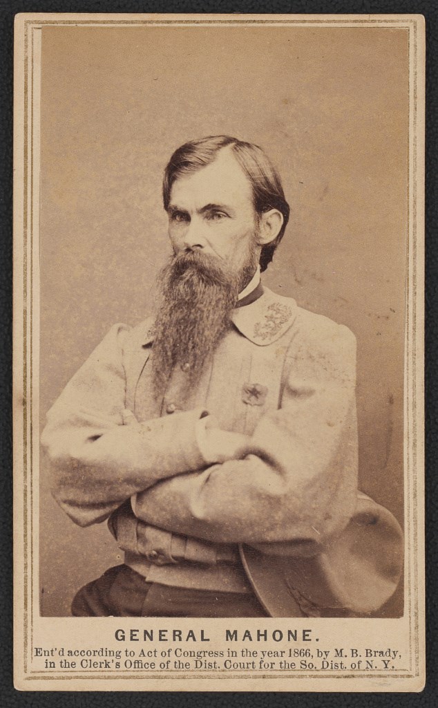 Black and white photo card showing a man in a gray coat with black hair and a beard seated on a chair