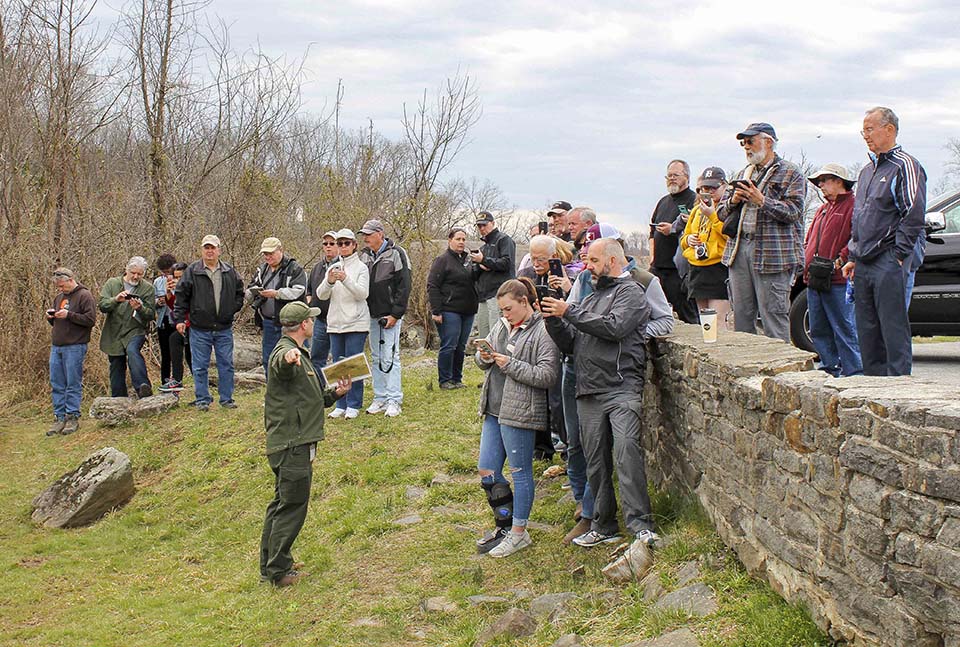A park ranger describes the location of a historic photo taken near Devil's Den in July, 1863 as visitors follow along via the Then and Now web page on their phones.