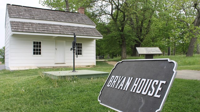 A small white building made of painted wooden planks. A sign in front says "Bryan Farm"