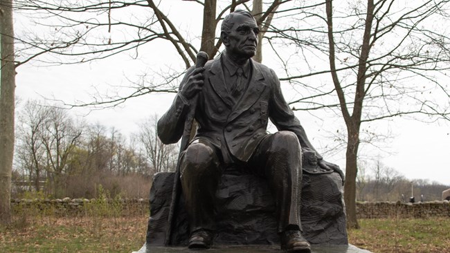 A bronze monument of a man wearing civilian clothes, looking downward and across the field in front