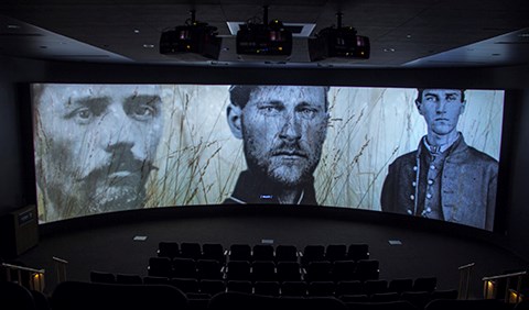 The film, A New Birth of Freedom, is playing inside the theater. The scene depicts pictures of three soldiers who fought in the battle.