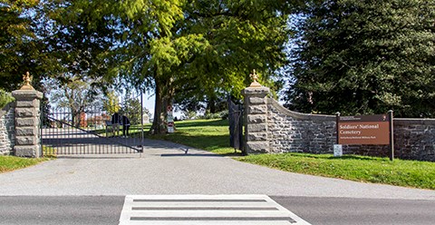 The Taneytown Road entrance into the Soldiers' National Cemetery. A black iron gate, stone wall, and entrance sign are welcome visitors.