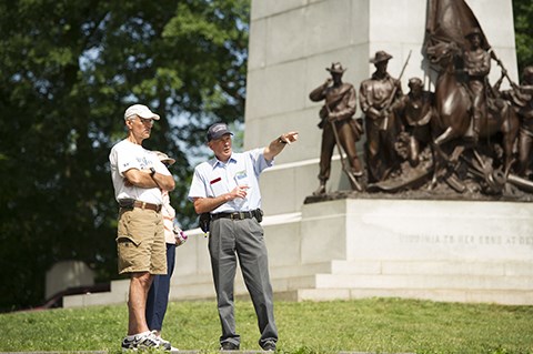 A Licensed Battlefield Guide gives a tour of the battlefield at the Virginia memorial. One guide and two visitors stand near the Virginia memorial.