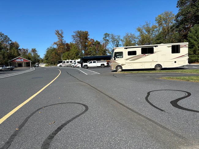 A parking lot with several RVs and buses parked in large parking spaces. A small stone building is to the left