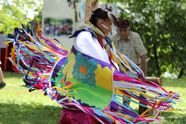 indigenous person in colorful regalia dancing in the memorial area of the park