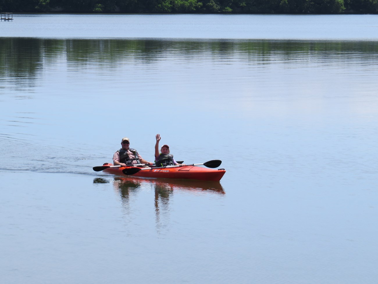 A young girl in a kayak waves to the camera.