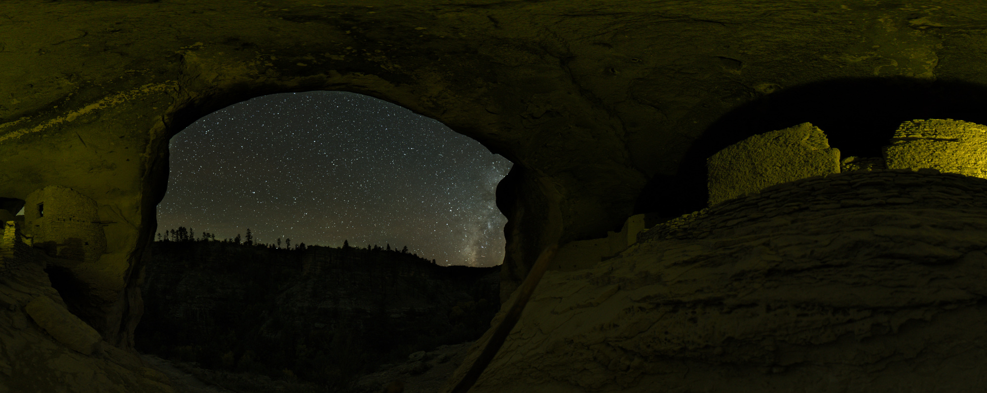 Standing on the landing of Cave 4 and looking 360 degrees, the cave walls are artificially lit and open out to a view of the Milky Way galaxy over Cliff Dweller Canyon.