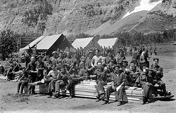group of young men holding camp cookware, canvas tents in background