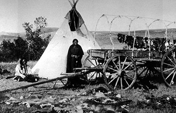 animal hides spread about two native people, a tipi, and wagon