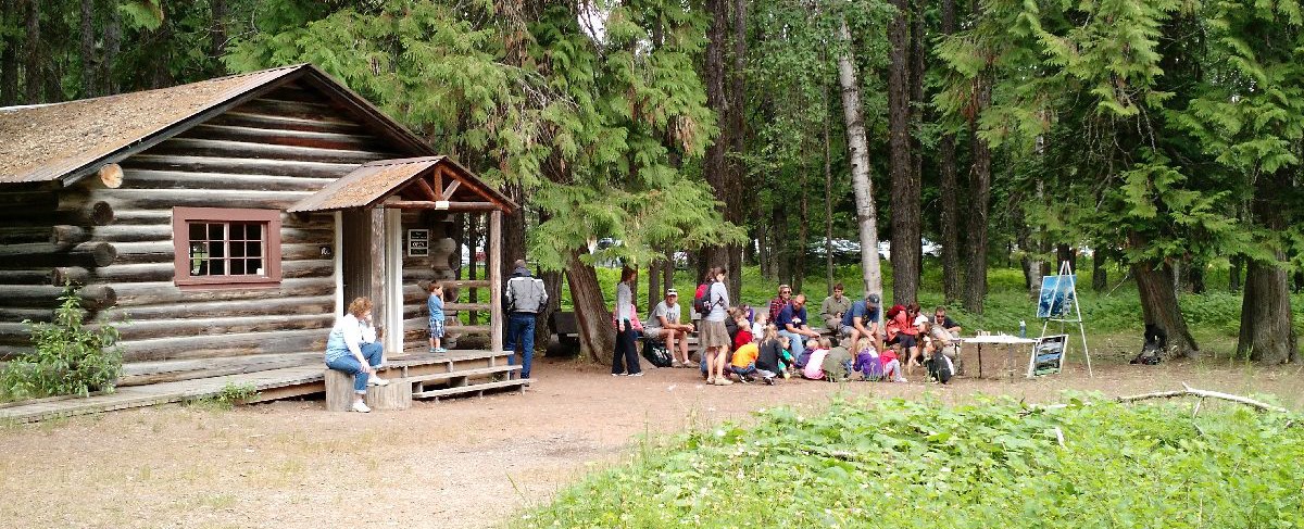 Group of children and adults outside small cabin in forest setting