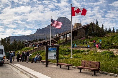 Parking lot in front of large building with American and Canadian flags and a lot of people.