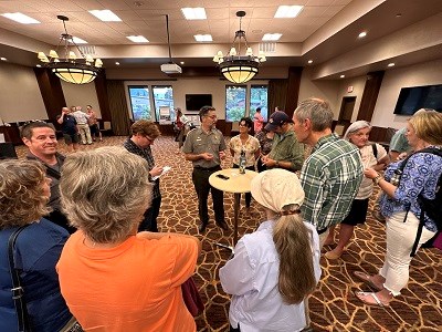 People standing around a small cocktail table listening to a person in park service uniform.