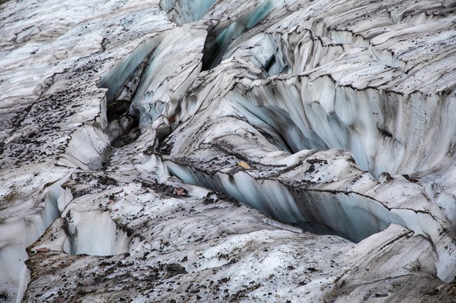 Swirling ice from a glacier is lined with dark rock sediment.