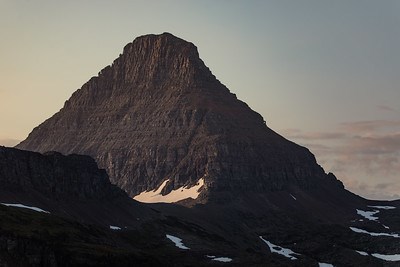 A dark brown mountain with nearly vertical sides is illuminated by a golden sunrise.