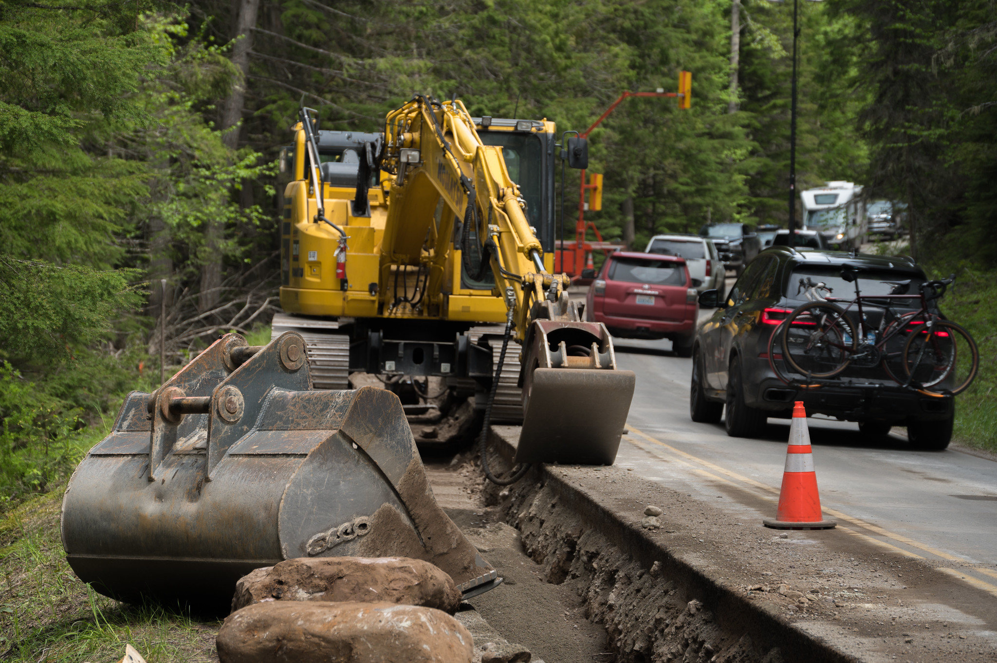 Road construction equipment parked on Going-to-the-Sun Road near Lake McDonald. Cars driving by in opposite lane.