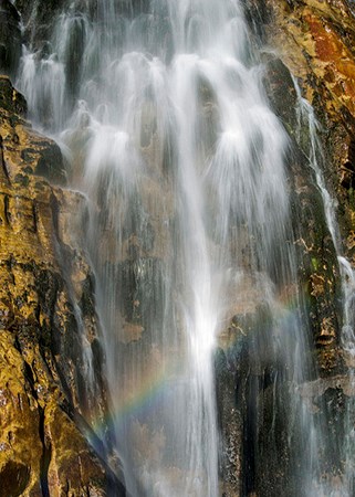 water falling over rocks with rainbow in droplets
