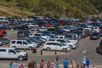 A very full parking lot in the mountains with crowds of people around.